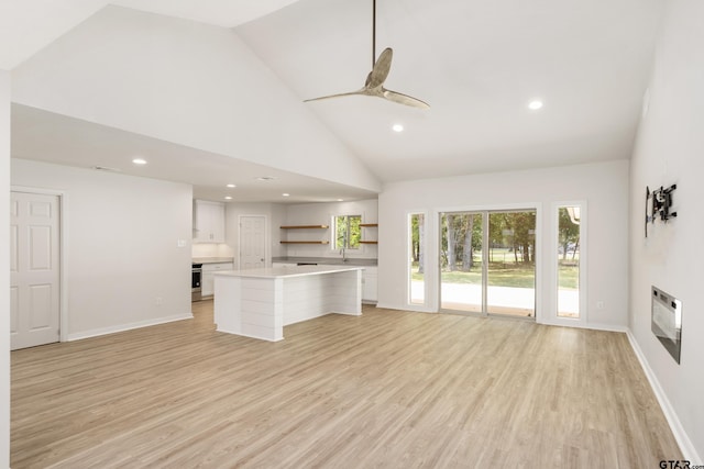 unfurnished living room with heating unit, ceiling fan, high vaulted ceiling, sink, and light hardwood / wood-style flooring