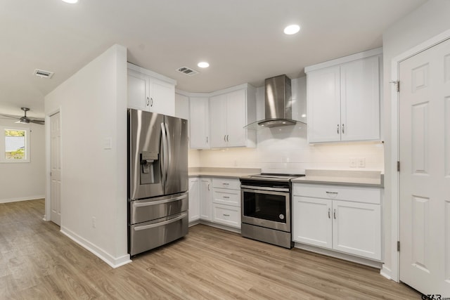 kitchen featuring stainless steel appliances, wall chimney range hood, light wood-type flooring, white cabinetry, and ceiling fan