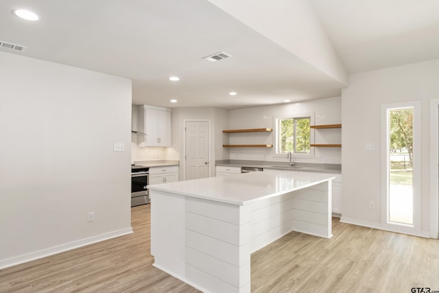 kitchen with stainless steel electric range oven, a kitchen island, light wood-type flooring, white cabinets, and sink