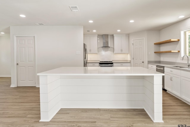 kitchen with sink, a kitchen island, wall chimney range hood, and white cabinetry