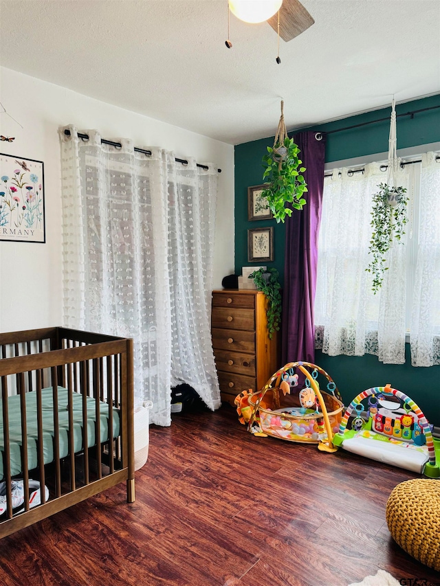 bedroom featuring a crib, a textured ceiling, hardwood / wood-style flooring, and ceiling fan