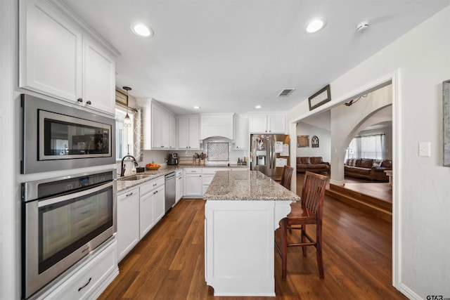 kitchen with sink, white cabinetry, decorative light fixtures, appliances with stainless steel finishes, and a kitchen island