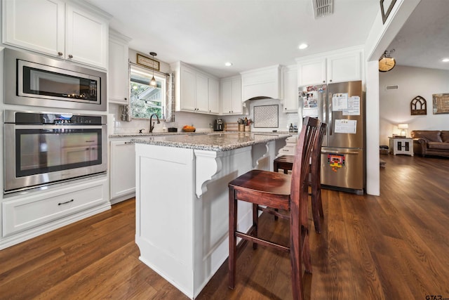 kitchen with white cabinetry, appliances with stainless steel finishes, a kitchen breakfast bar, a kitchen island, and light stone countertops