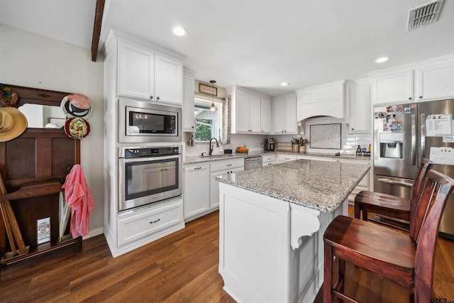 kitchen with appliances with stainless steel finishes, white cabinetry, a center island, light stone counters, and custom range hood