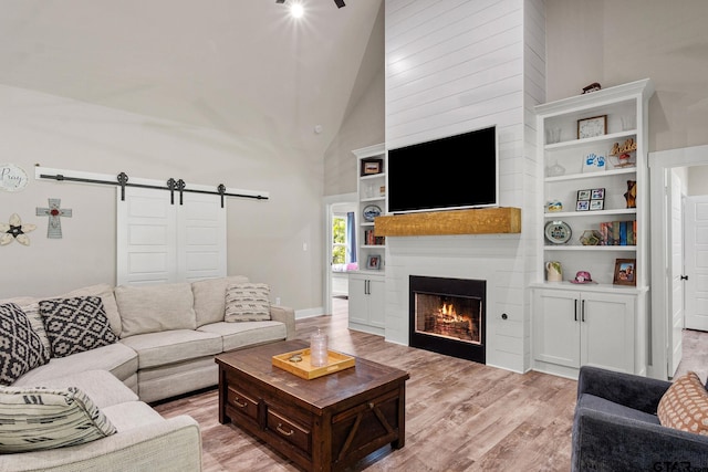 living room with a barn door, light hardwood / wood-style floors, and high vaulted ceiling