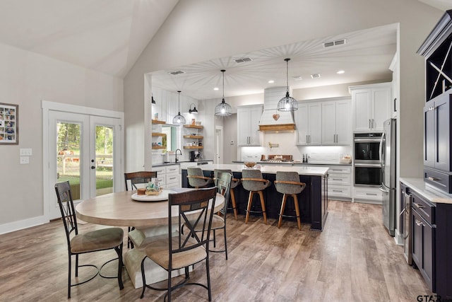 dining area with light hardwood / wood-style floors, french doors, sink, and high vaulted ceiling