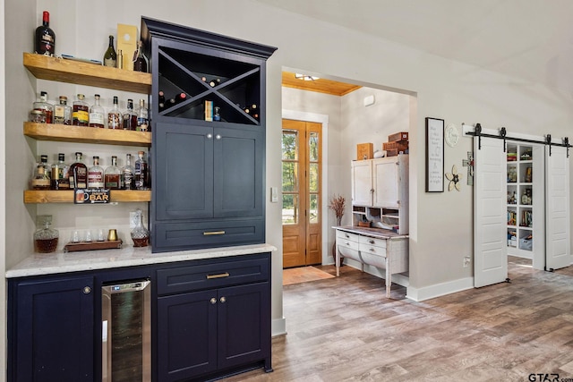 bar with a barn door, blue cabinetry, wine cooler, and light wood-type flooring