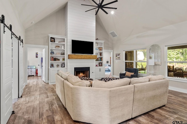 living room with a fireplace, a barn door, high vaulted ceiling, hardwood / wood-style flooring, and ceiling fan