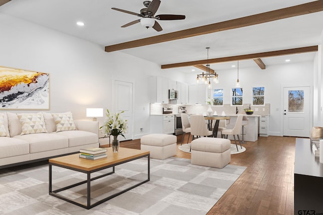 living room with beamed ceiling, ceiling fan with notable chandelier, and light hardwood / wood-style floors