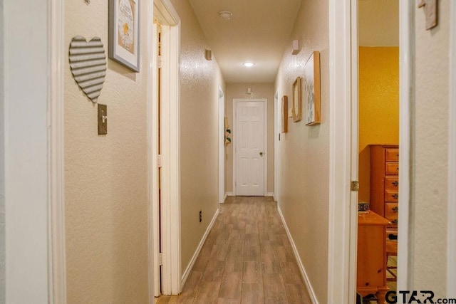 hall with a textured wall, baseboards, and wood finished floors