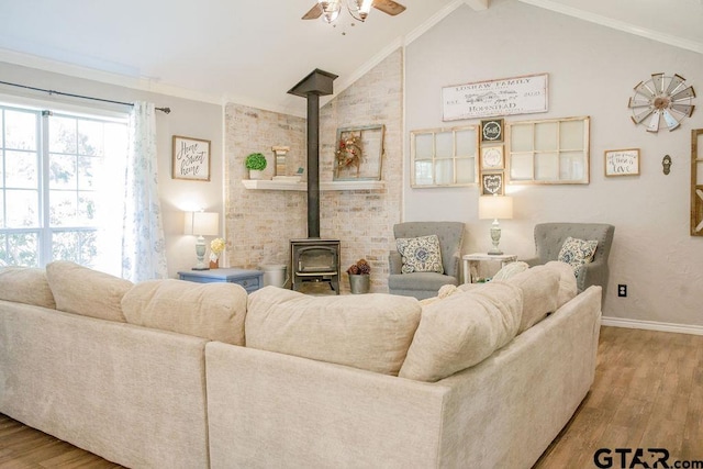 living area with baseboards, lofted ceiling, ceiling fan, wood finished floors, and a wood stove