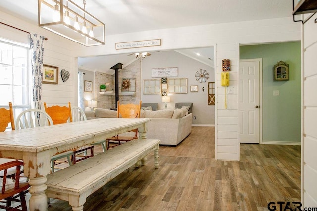 dining room featuring lofted ceiling, a wood stove, baseboards, and wood finished floors