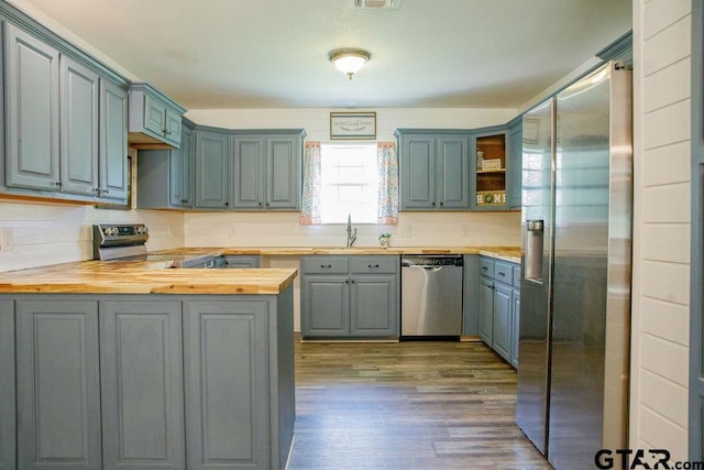 kitchen with a peninsula, wood finished floors, a sink, wooden counters, and appliances with stainless steel finishes