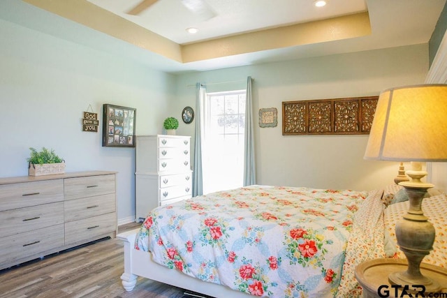 bedroom featuring a tray ceiling, wood finished floors, and recessed lighting