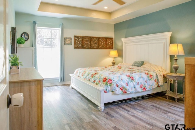 bedroom with a ceiling fan, a tray ceiling, recessed lighting, and wood finished floors