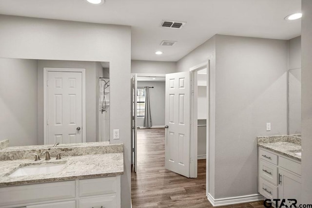 full bath with visible vents, baseboards, two vanities, wood finished floors, and a sink