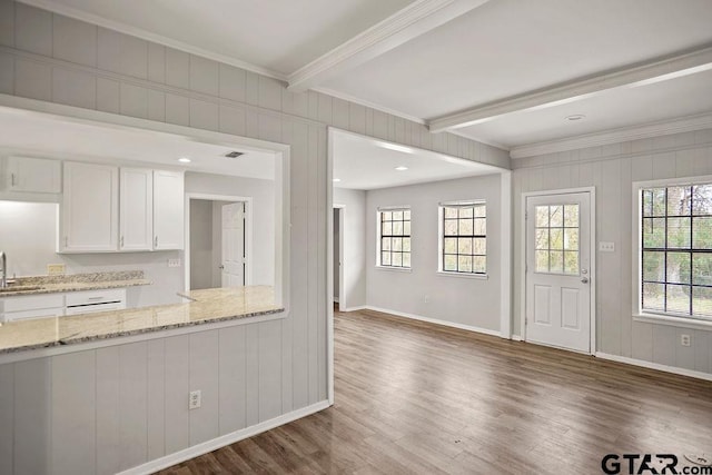 kitchen featuring light stone counters, wood finished floors, beam ceiling, ornamental molding, and white cabinets