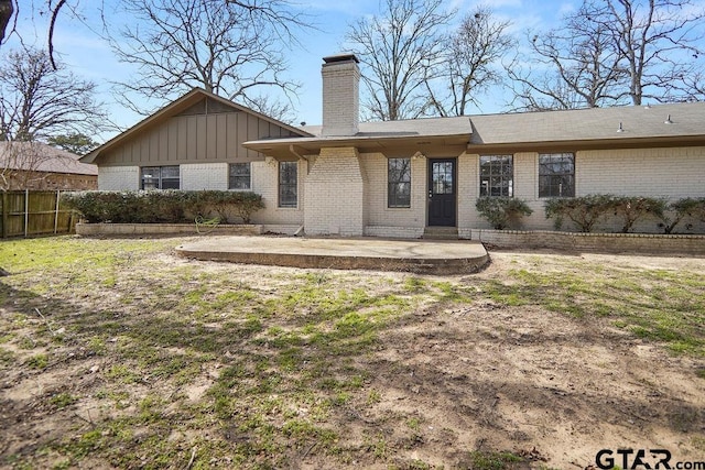 back of property with brick siding, board and batten siding, a chimney, and fence