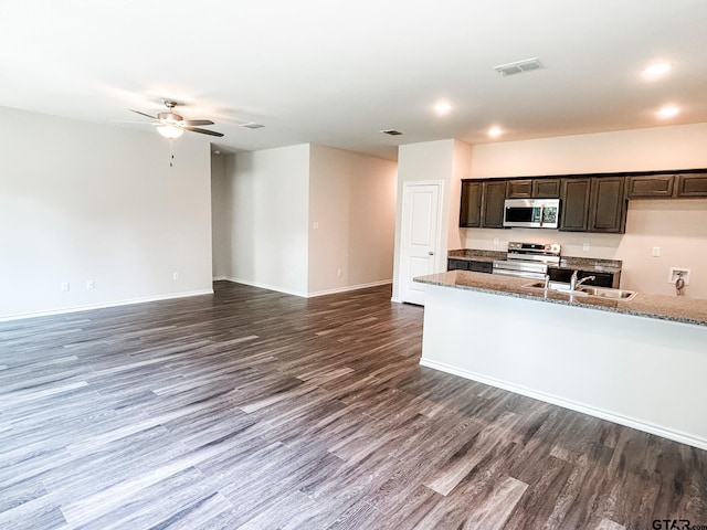 kitchen with sink, dark wood-type flooring, appliances with stainless steel finishes, dark brown cabinetry, and stone countertops