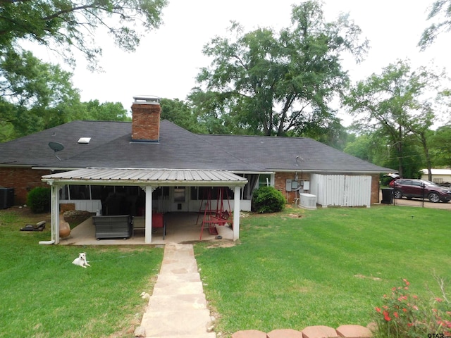 rear view of house featuring a patio, a shingled roof, a yard, and a chimney
