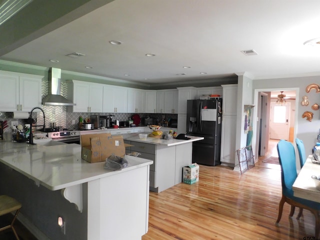 kitchen with black fridge, wall chimney exhaust hood, a center island, decorative backsplash, and light wood-type flooring