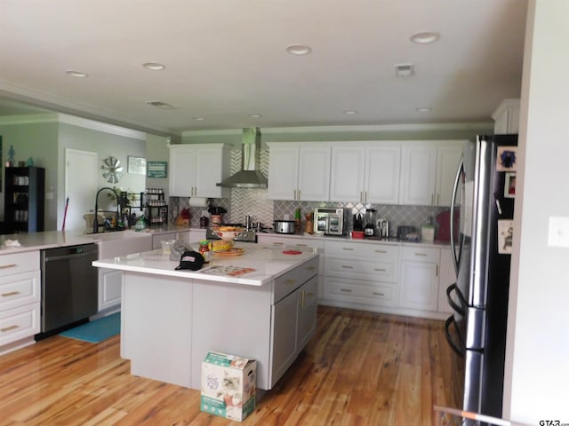 kitchen featuring wall chimney range hood, light countertops, freestanding refrigerator, ornamental molding, and black dishwasher