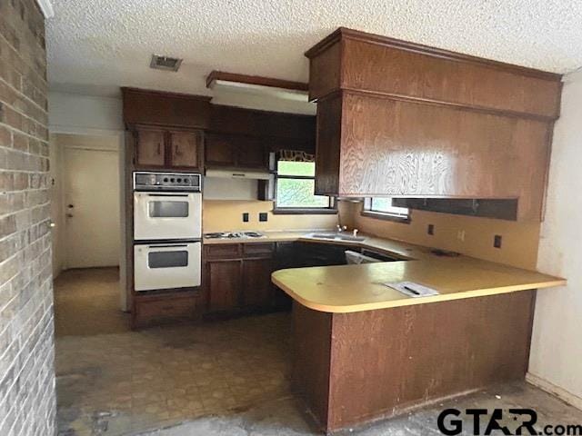 kitchen with white double oven, visible vents, stainless steel gas cooktop, a peninsula, and a textured ceiling