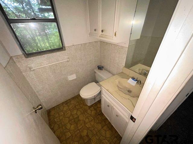 half bath with tile walls, toilet, vanity, and a wainscoted wall
