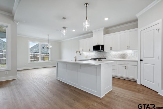 7130 Alexander Dr, Tyler, TX 75707 - kitchen featuring stainless steel microwave, crown molding, backsplash, an island with sink, and light wood-style floors