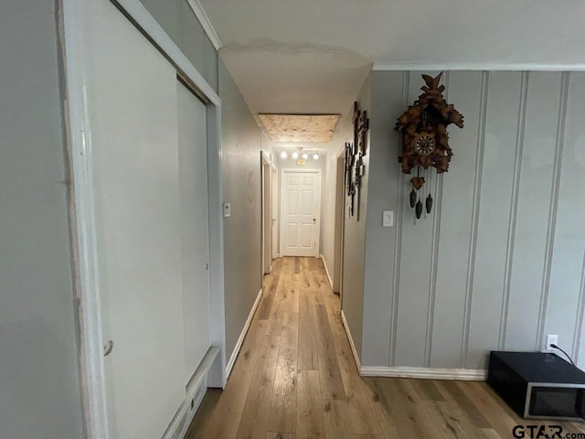 corridor featuring baseboards, light wood-style floors, and a decorative wall