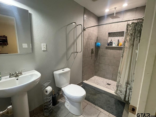 bathroom featuring tile patterned flooring, toilet, a textured wall, a shower stall, and a sink