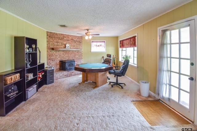 rec room with a wealth of natural light, ceiling fan, parquet floors, and a wood stove