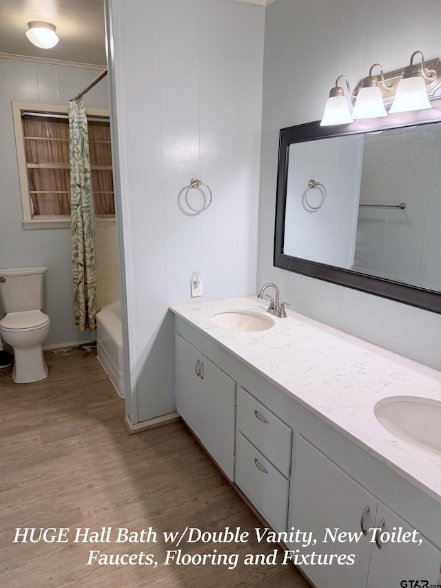 full bath with double vanity, wood finished floors, a sink, and shower / bath combo with shower curtain