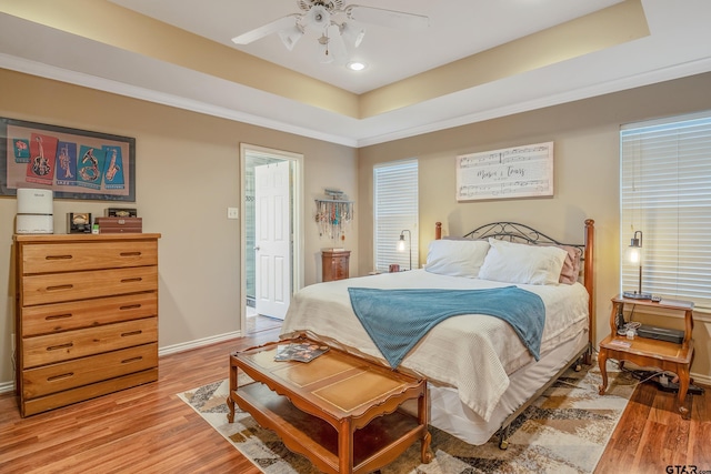 bedroom featuring hardwood / wood-style floors, ensuite bathroom, ornamental molding, ceiling fan, and a tray ceiling