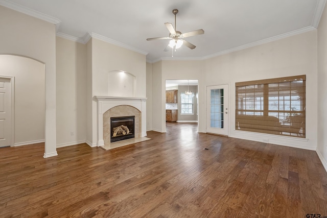 unfurnished living room with ceiling fan, arched walkways, a fireplace, wood finished floors, and ornamental molding