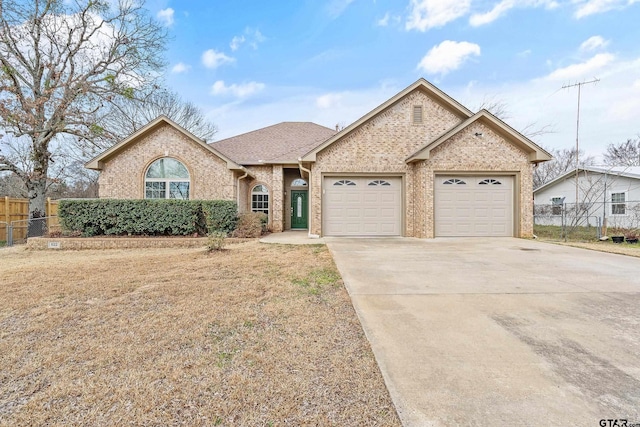 view of front of property with brick siding, driveway, an attached garage, and fence