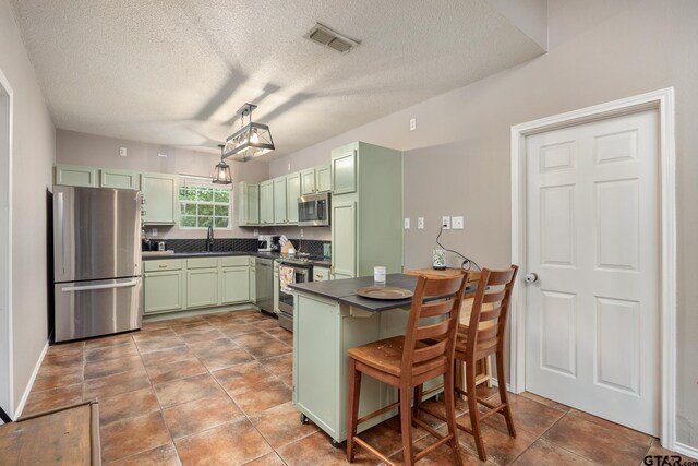 1805 San Saba Dr, Bullard, TX 75757 - kitchen with green cabinetry, stainless steel appliances, dark countertops, a textured ceiling, and a breakfast bar area