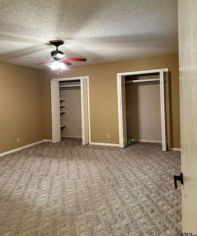 unfurnished bedroom with ceiling fan, a textured ceiling, and two closets