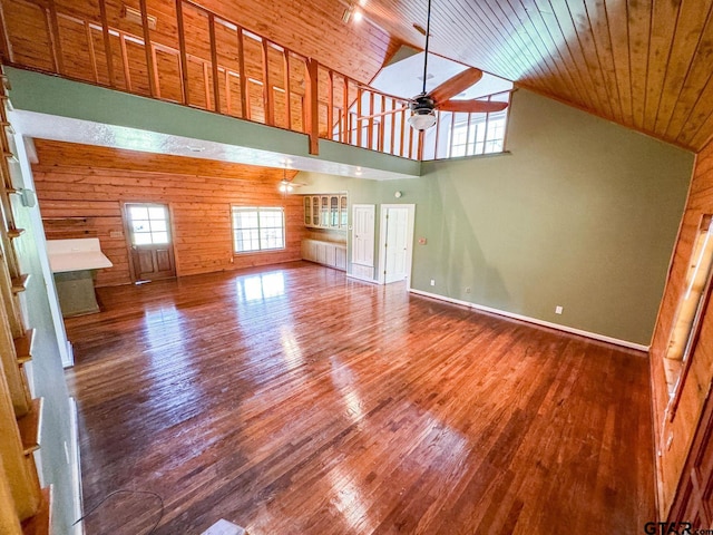 unfurnished living room featuring wooden ceiling, ceiling fan, high vaulted ceiling, hardwood / wood-style floors, and wooden walls