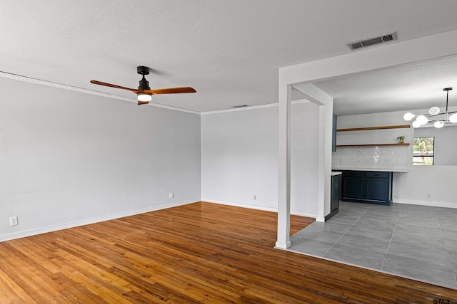 unfurnished living room featuring ceiling fan with notable chandelier, dark hardwood / wood-style floors, a textured ceiling, and crown molding