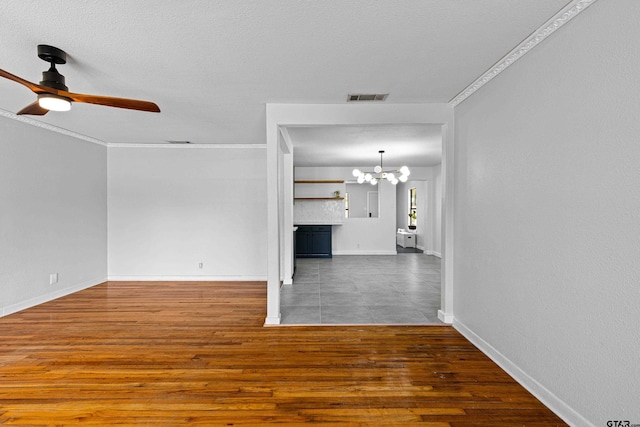 unfurnished living room featuring ornamental molding, ceiling fan with notable chandelier, dark wood-type flooring, and a textured ceiling