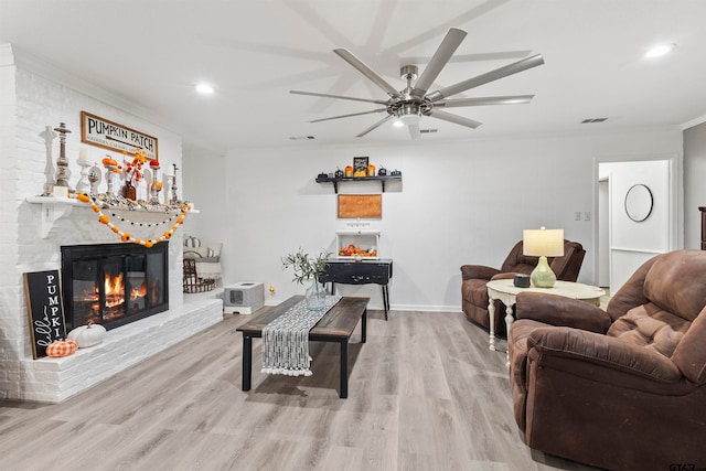 living room featuring light hardwood / wood-style flooring, ceiling fan, ornamental molding, and a brick fireplace