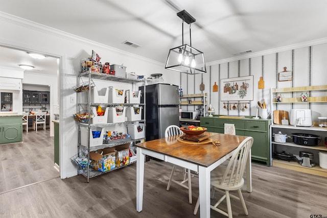 kitchen with appliances with stainless steel finishes, green cabinetry, hanging light fixtures, wood-type flooring, and crown molding