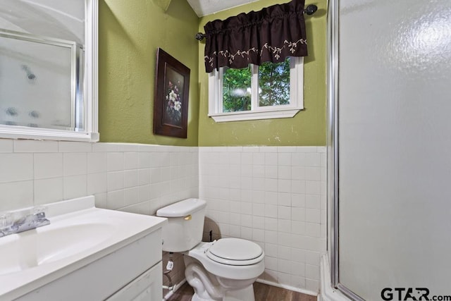 bathroom with vanity, toilet, tile walls, a wainscoted wall, and a stall shower