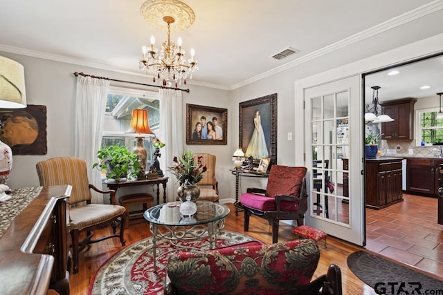 living area with visible vents, crown molding, wood finished floors, and an inviting chandelier