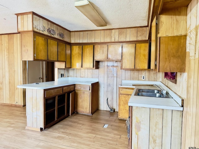 kitchen with sink, kitchen peninsula, light hardwood / wood-style floors, a textured ceiling, and wooden walls