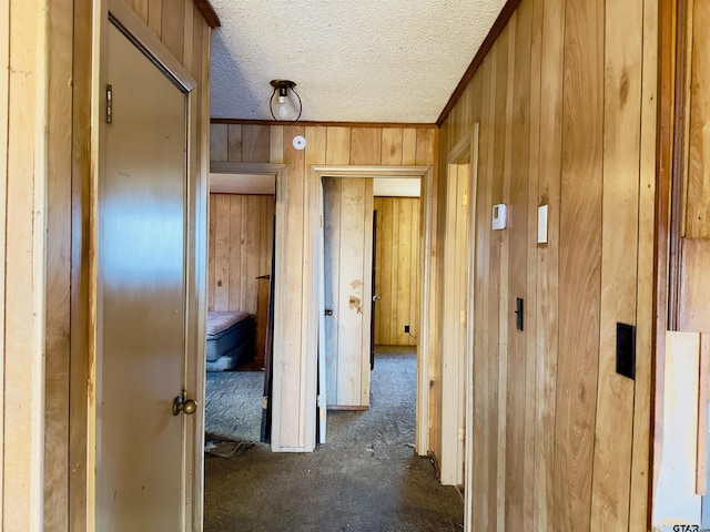 hallway featuring dark colored carpet, a textured ceiling, and wooden walls