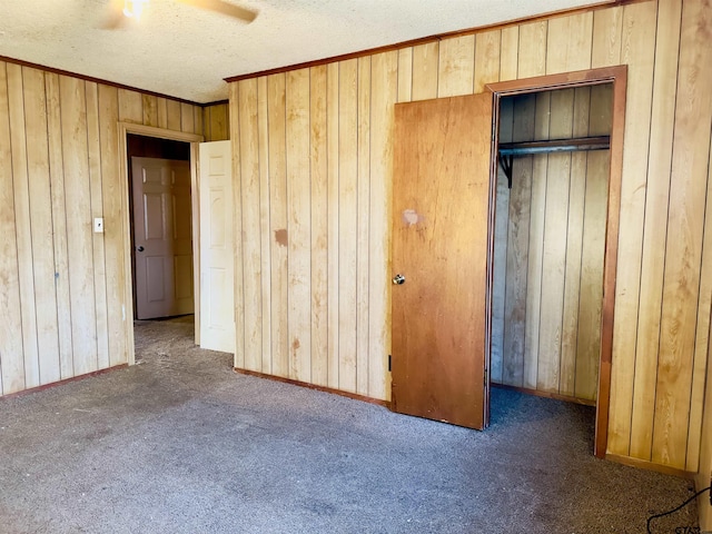 unfurnished bedroom featuring dark colored carpet, ceiling fan, a textured ceiling, and wooden walls