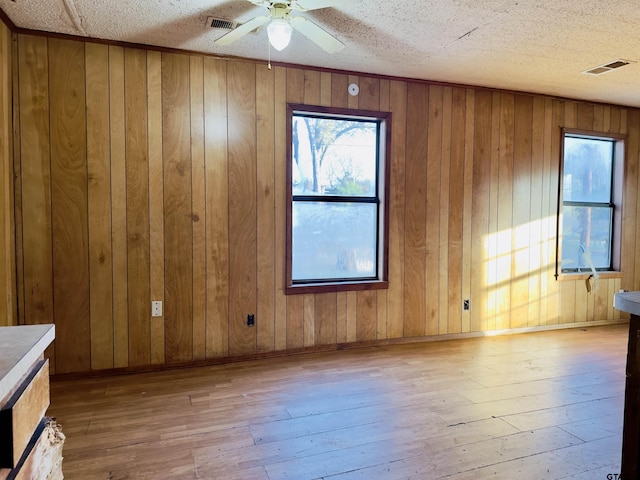 interior space featuring ceiling fan, light wood-type flooring, a textured ceiling, and wooden walls