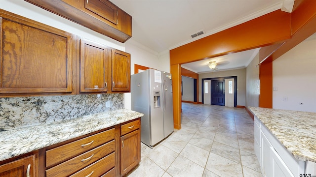 kitchen with light stone counters, stainless steel refrigerator with ice dispenser, backsplash, crown molding, and light tile patterned floors